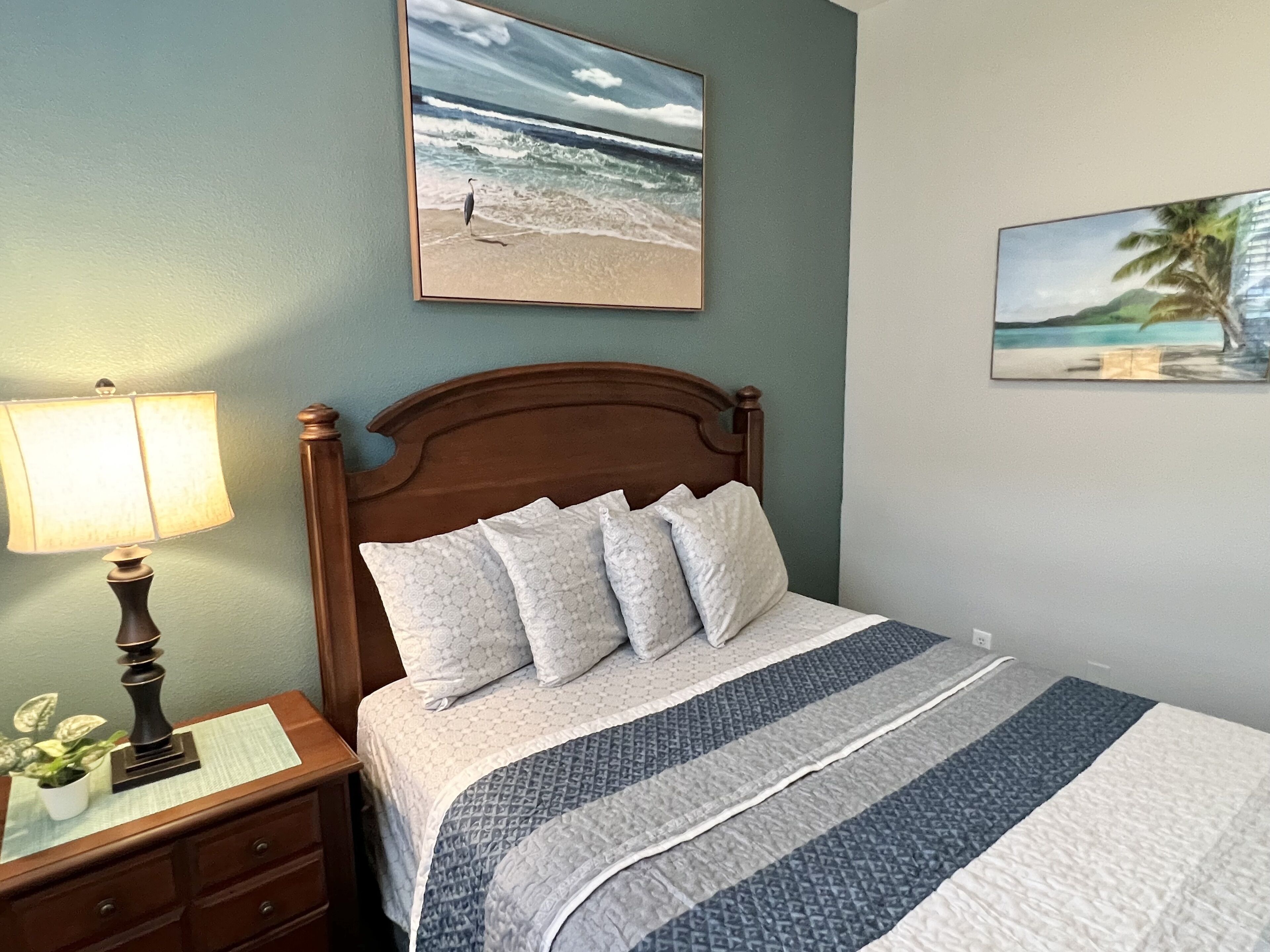 A neatly made bed with a patterned bedspread, a wooden headboard, and a nightstand with a lamp and a small plant.