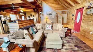 A cozy cabin interior with a sectional sofa, a small ottoman, a wooden coffee table, and a red door.