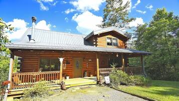 A log cabin with a porch, a chimney, and a small deck.