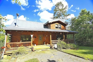 A log cabin with a porch, a chimney, and a small deck.