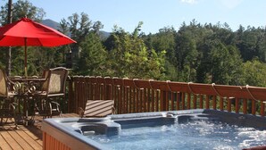 A hot tub on a wooden deck with a red umbrella, surrounded by chairs and a wooden fence. - Bison Overlook Lodge: on a 65-acre bison ranch (Clyde)