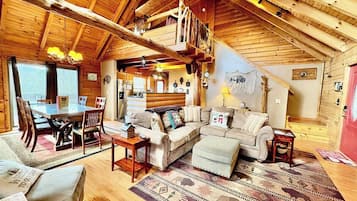 A cozy interior with a wooden ceiling, a dining area with a table and chairs, a sofa, and a patterned rug.