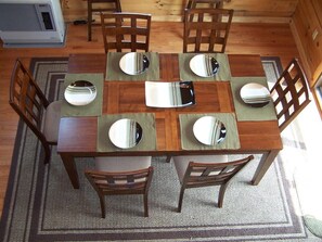 A wooden dining table with six chairs, each with a reflective placemat.