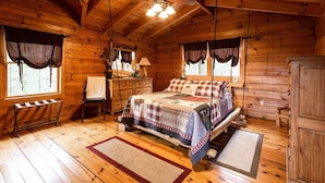 A wooden cabin bedroom with a bed, a chair, a nightstand, a lamp, and a ceiling fan. - Bison Overlook Lodge: on a 65-acre bison ranch (Clyde)