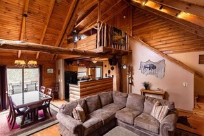 A log cabin interior with a dining area, a large sofa, and a kitchen. - Bison Overlook Lodge: on a 65-acre bison ranch (Clyde)