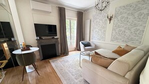 A living room with a sofa, a TV, a fireplace, a dining table, and a chandelier.