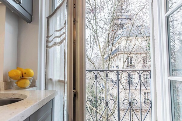 A kitchen with a bowl of lemons on the counter, a window with a view of a building and trees.