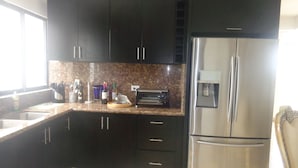 Una cocina moderna con armarios oscuros, un refrigerador de acero inoxidable, horno empotrado y encimera de granito.