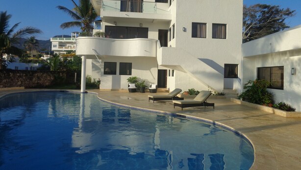 Un edificio moderno de varios pisos con piscina, sillones de descanso y plantas en macetas.
