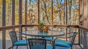 Un espace extérieur abrité, doté d’une table ronde et de quatre chaises, entouré d’une terrasse en bois et d’une clôture en treillis métallique.