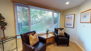 A living room with two leather armchairs, a coffee table, and a large window with blinds. - Terracehouse - Steps to Slopes - Hot Tub/Pool - ASE Transportation (Snowmass Village)