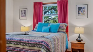 Un lit recouvert d’une couvre-lit à motifs, deux oreillers bleus et des rideaux rouges. Il y a deux tables de chevet avec des lampes, une de chaque côté du lit.