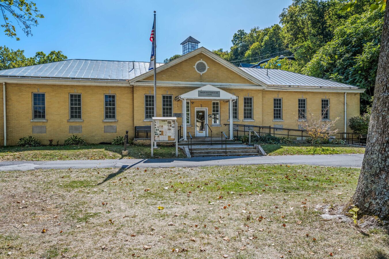 A yellow brick building with a central entrance, a flagpole, and a sign reading "Main Bathhouse".