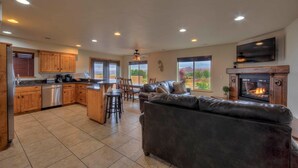 A spacious living area with a leather sofa, a fireplace, and a kitchen with wooden cabinets and a dining area. - SG3 Private hot tub, Ping pong, Badminton, Huge Patio, Views (Moab)