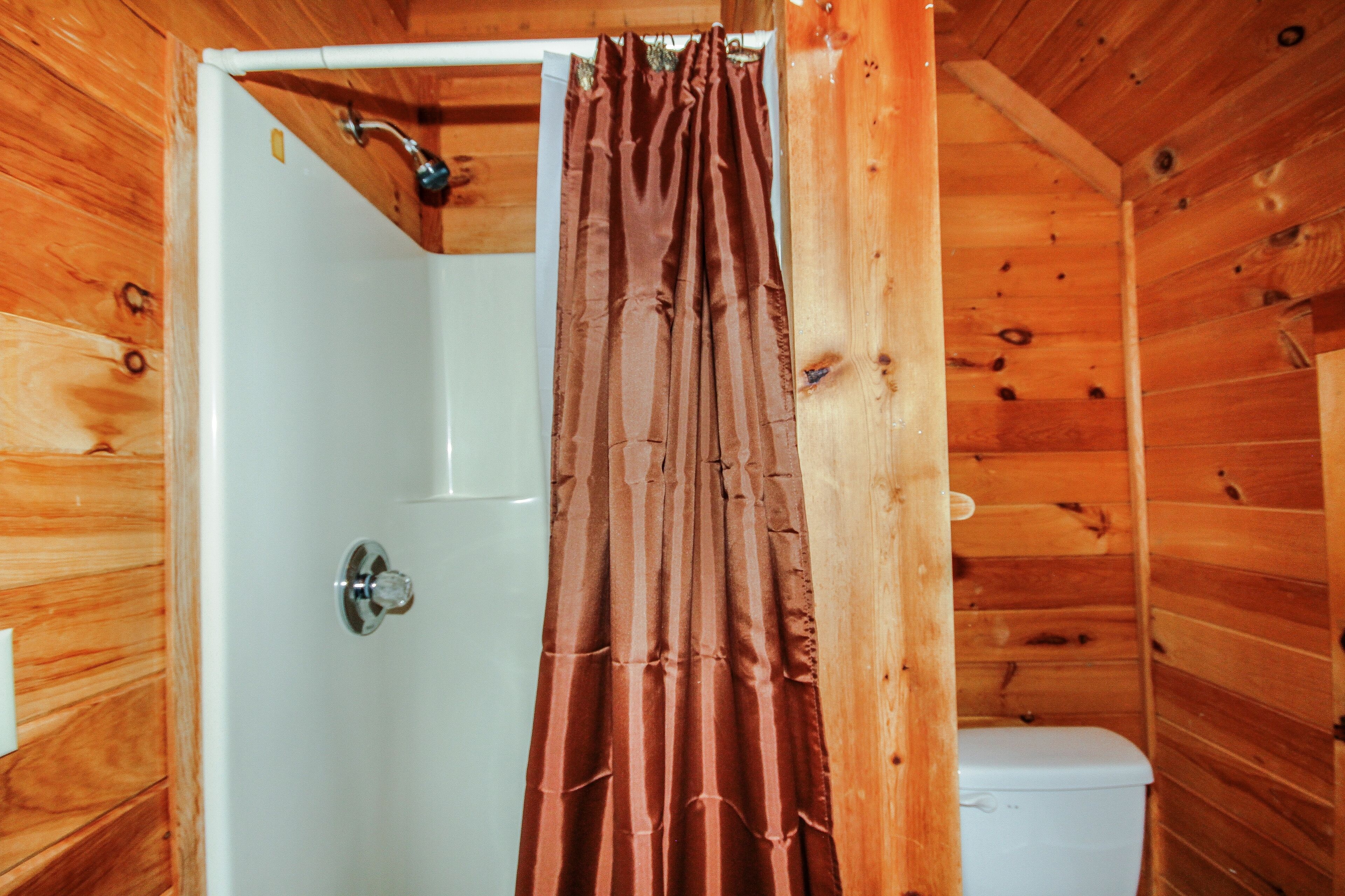 A wooden cabin bathroom with a shower curtain, a toilet, and a visible showerhead.