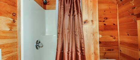 A wooden cabin bathroom with a shower curtain, a toilet, and a visible showerhead.