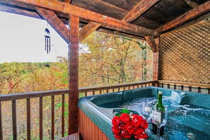 Un bain à remous décoré de roses et une bouteille de vin, une terrasse en bois et une vue sur les arbres.