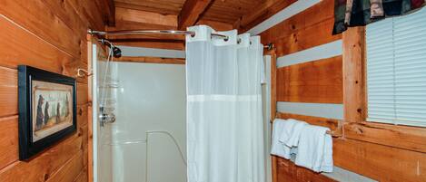 Baño de cabaña de madera con ducha, un cuadro enmarcado en la pared y una ventana con persianas.