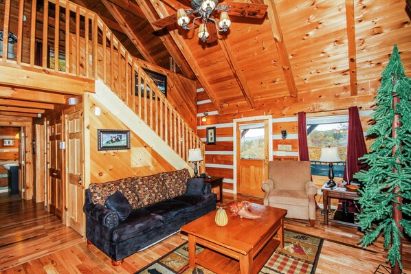 L'intérieur d'un chalet en bois, avec un canapé, un fauteuil et un sapin de Noël.