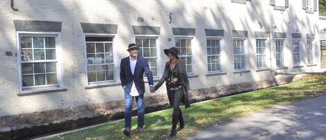 A man and woman holding hands walking on a sidewalk next to a building with multiple windows and a stone foundation.