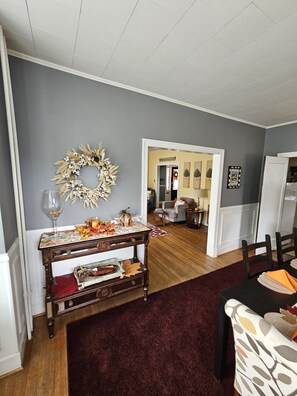 A dining area with a table set for two, a decorative console table with glassware and a centerpiece, and a hallway leading to another room. - Aunt Beas Bungalow - Pets, hot tub, screen porch, wifi, fenced yard, king bed, town (Berkeley Springs)