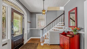 Un couloir avec un plancher en bois, une armoire rouge ornée de fleurs, un radiateur blanc et un escalier avec des rampes blanches.