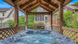 Un bain à remous sous une pergola en bois, avec vue sur les maisons au loin.