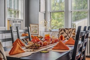 Una mesa de comedor dispuesta con servilletas anaranjadas, un florero de vidrio con flores secas y un centro de mesa con calabaza y hojas otoñales.