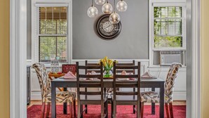 Une salle à manger avec une table en bois foncé, quatre chaises, un vase de fleurs jaunes et une horloge murale.