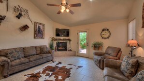 A living room with a brown leather sofa, a brown leather armchair, a fireplace, a ceiling fan, and a cowhide rug. - DW6  Private Hot Tub, En-Suite Bathroom for Each Bedroom, Near Arches Park! (Moab)