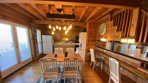Um interior em madeira com uma mesa de jantar, cadeiras, área de cozinha e um espelho grande.