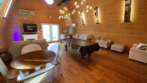 Uma sala de estar acolhedora, com piso de madeira, mesa redonda, sofás e luminárias pendentes.