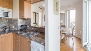 A modern kitchen with granite countertops, a Bosch dishwasher, and wooden cabinets. - Amazing Balcony and Pinch-Yourself Eiffel Views! (Paris)