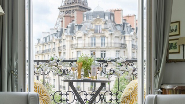 A balcony with a table set for two, featuring a bottle of wine, a glass, and a vase with flowers. A striped cushion is visible on the sofa. - Amazing Balcony and Pinch-Yourself Eiffel Views! (Paris)
