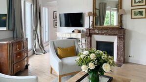 A living room with a television, a fireplace, a sofa, and a wooden cabinet. - Amazing Balcony and Pinch-Yourself Eiffel Views! (Paris)