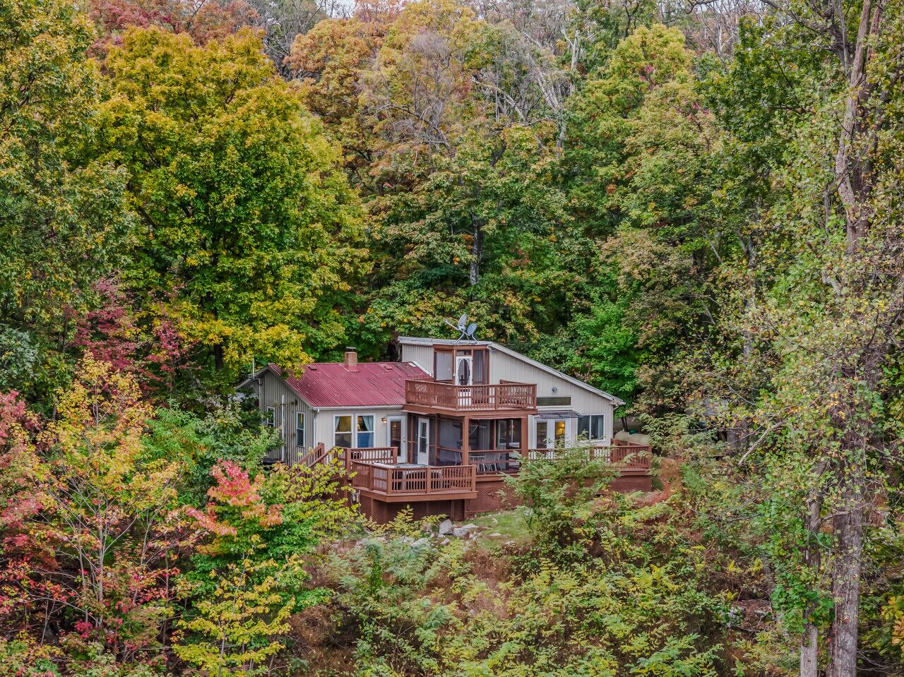 A two-story house with a deck, surrounded by dense forest.