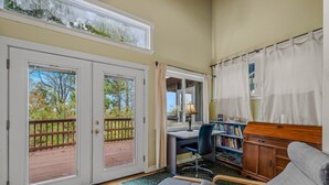 Una habitación con escritorio, silla, estantería y vistas a una terraza de madera a través de puertas de vidrio.