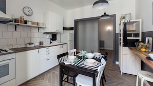 A modern kitchen with white cabinetry, a wooden countertop, and a dining area with a black table and white chairs. - Pannonia Smart House (Rome)