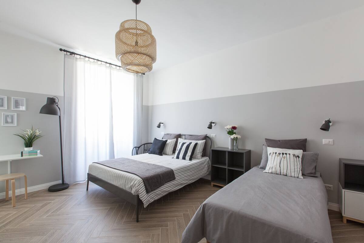 A modern bedroom with two beds, a desk, a chair, and a floor lamp.