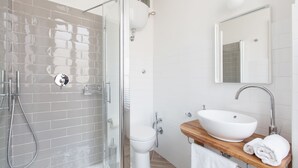 A modern bathroom with a glass-enclosed shower, a white toilet, and a wooden vanity with a large sink and a mirror above it. - Pannonia Smart House (Rome)