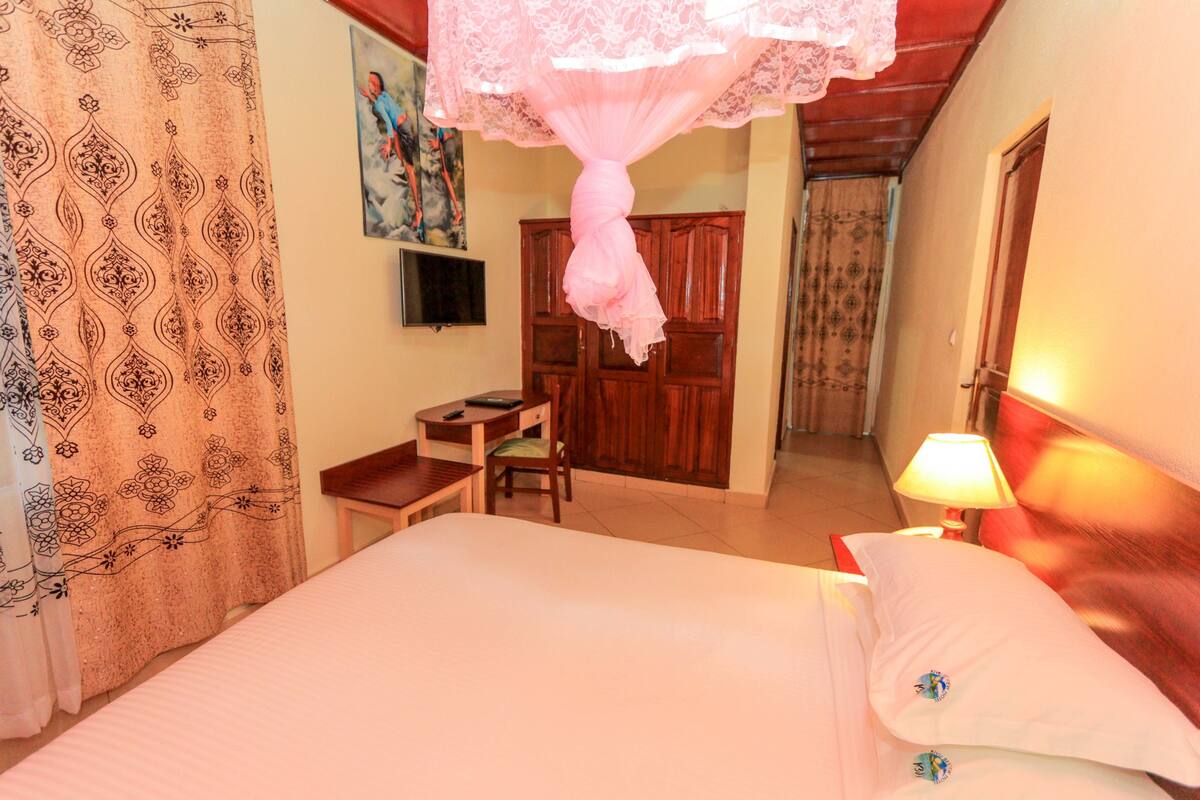A hotel room with a bed, a desk, a chair, a television, and a door.