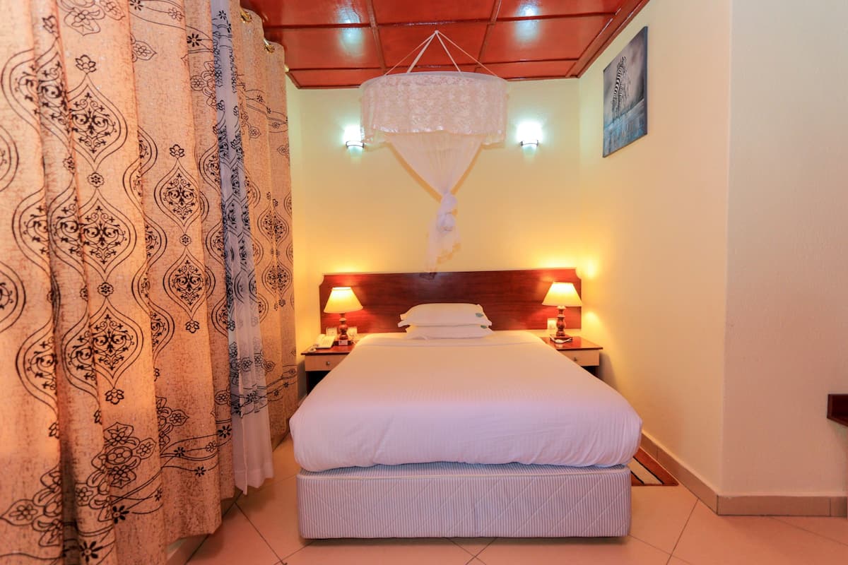 A neatly made bed with white linens, a hanging light fixture, and two bedside lamps.