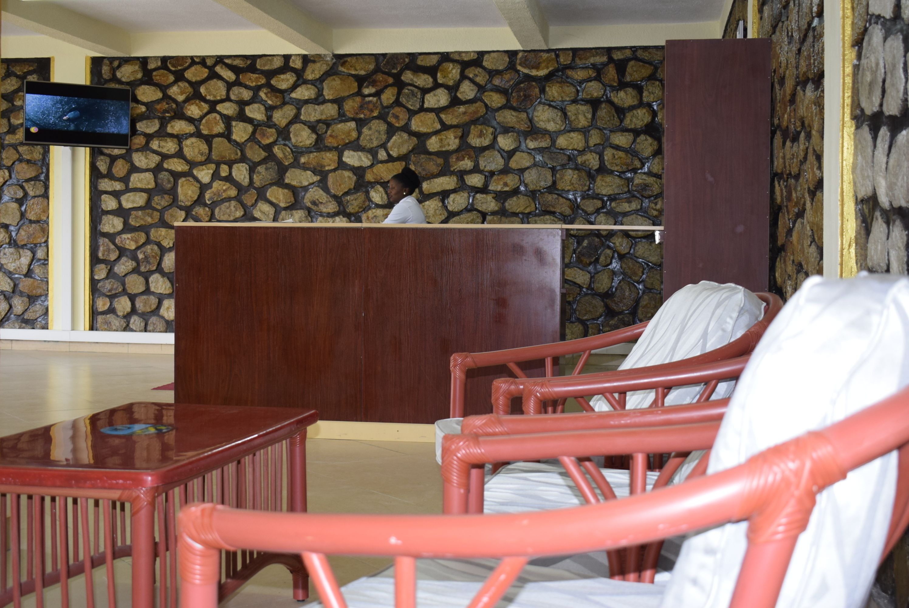 A reception area with a stone wall, a wooden reception desk, and red wicker chairs.
