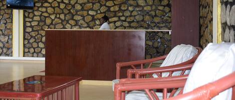 A reception area with a stone wall, a wooden reception desk, and red wicker chairs.