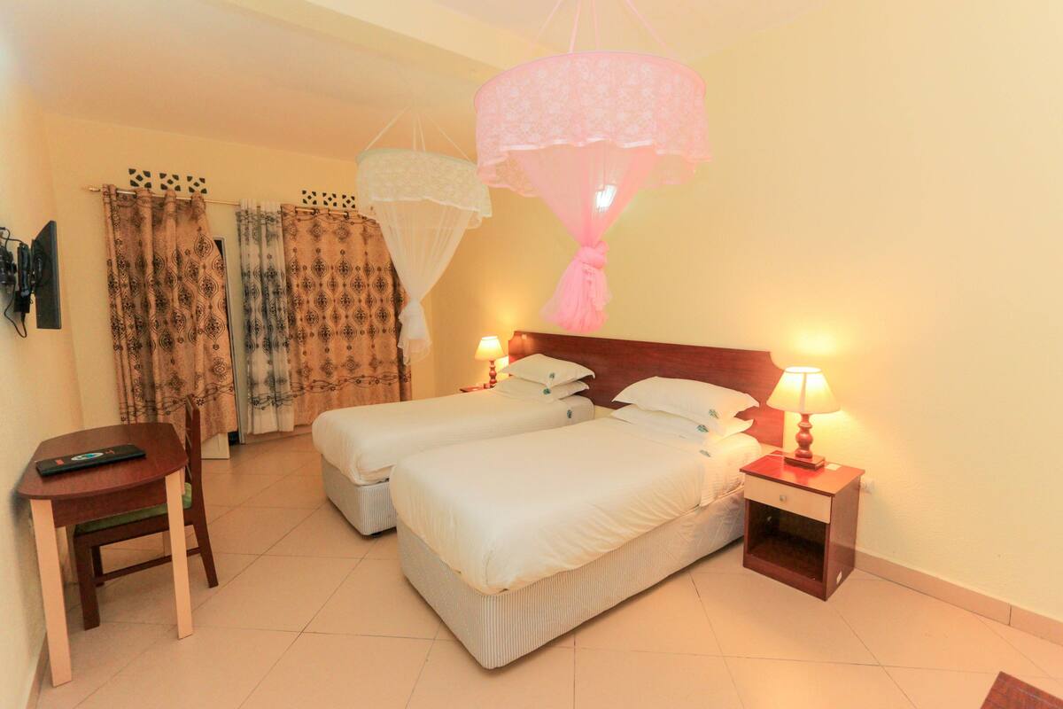 A hotel room with two beds, a desk, and a chair. There are two bedside tables with lamps.