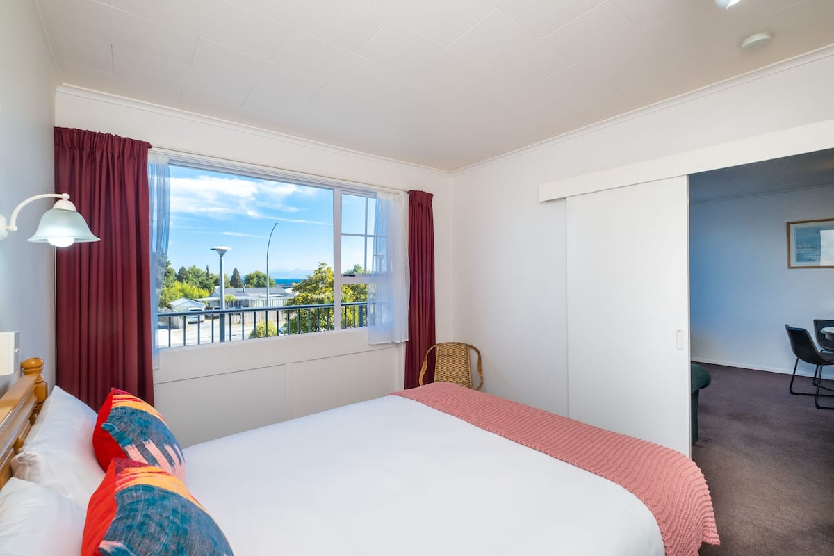 A hotel room with a bed, a chair, a desk, and a window with a view of the outdoors.