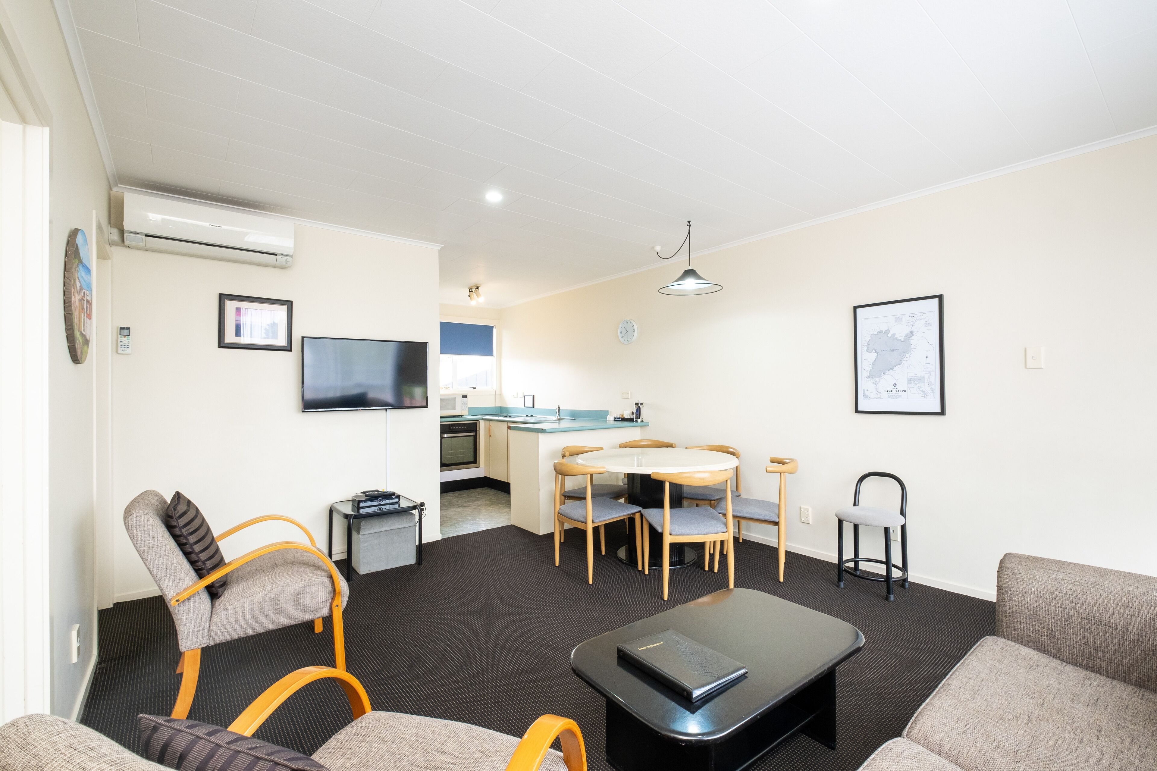 Un espacio habitable compacto con sofá, una mesita de centro, una mesa de comedor con sillas, un televisor en la pared y una kitchenette al fondo.