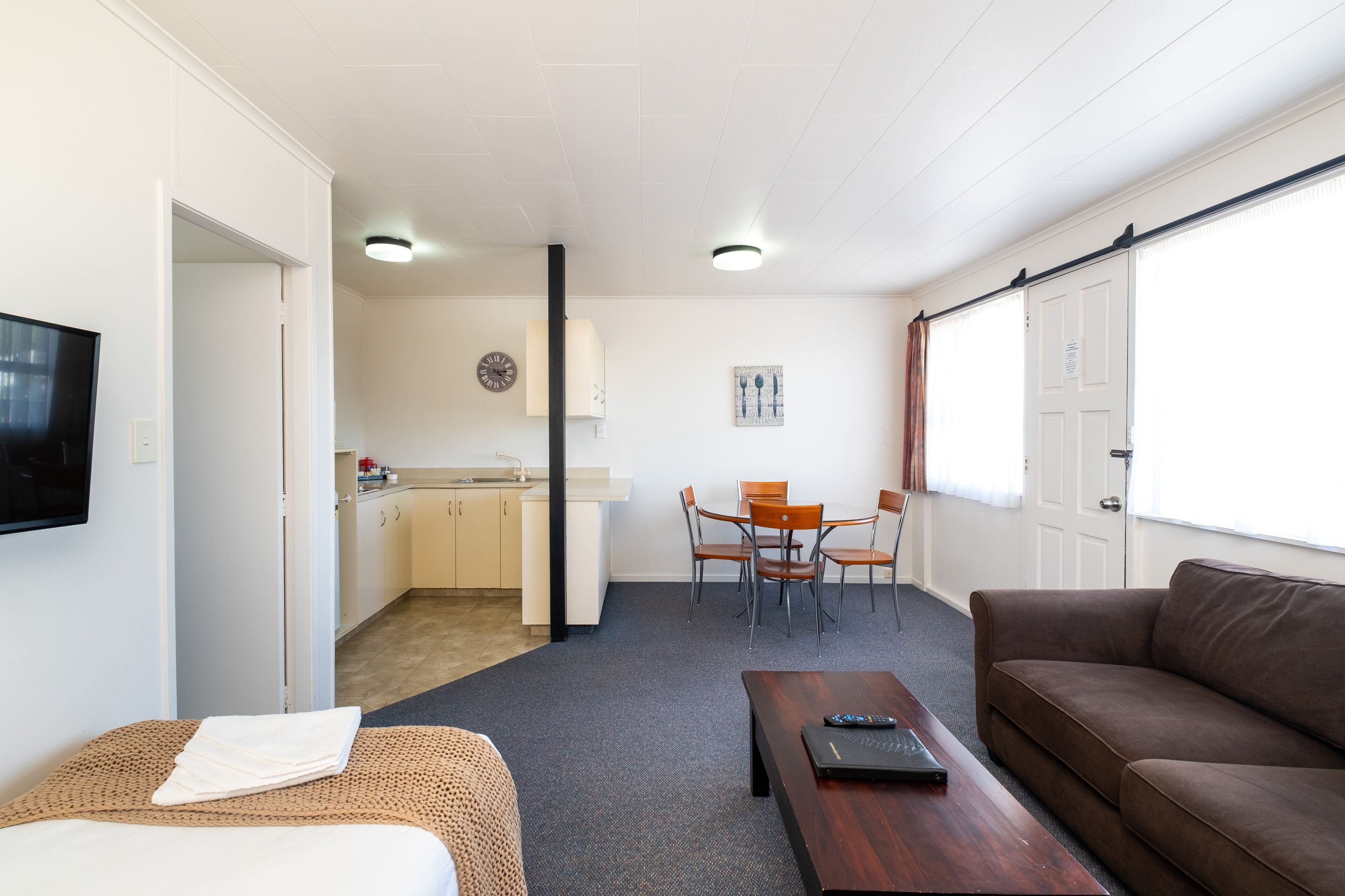 Ett kompakt bostadsutrymme med en soffa, ett litet bord, en TV, en liten köksdel och en matplats.