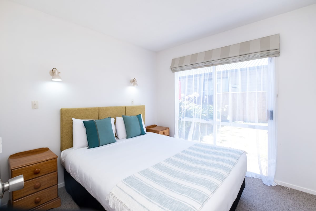 A bedroom with a bed, bedside tables, a nightstand, and a window with a view.