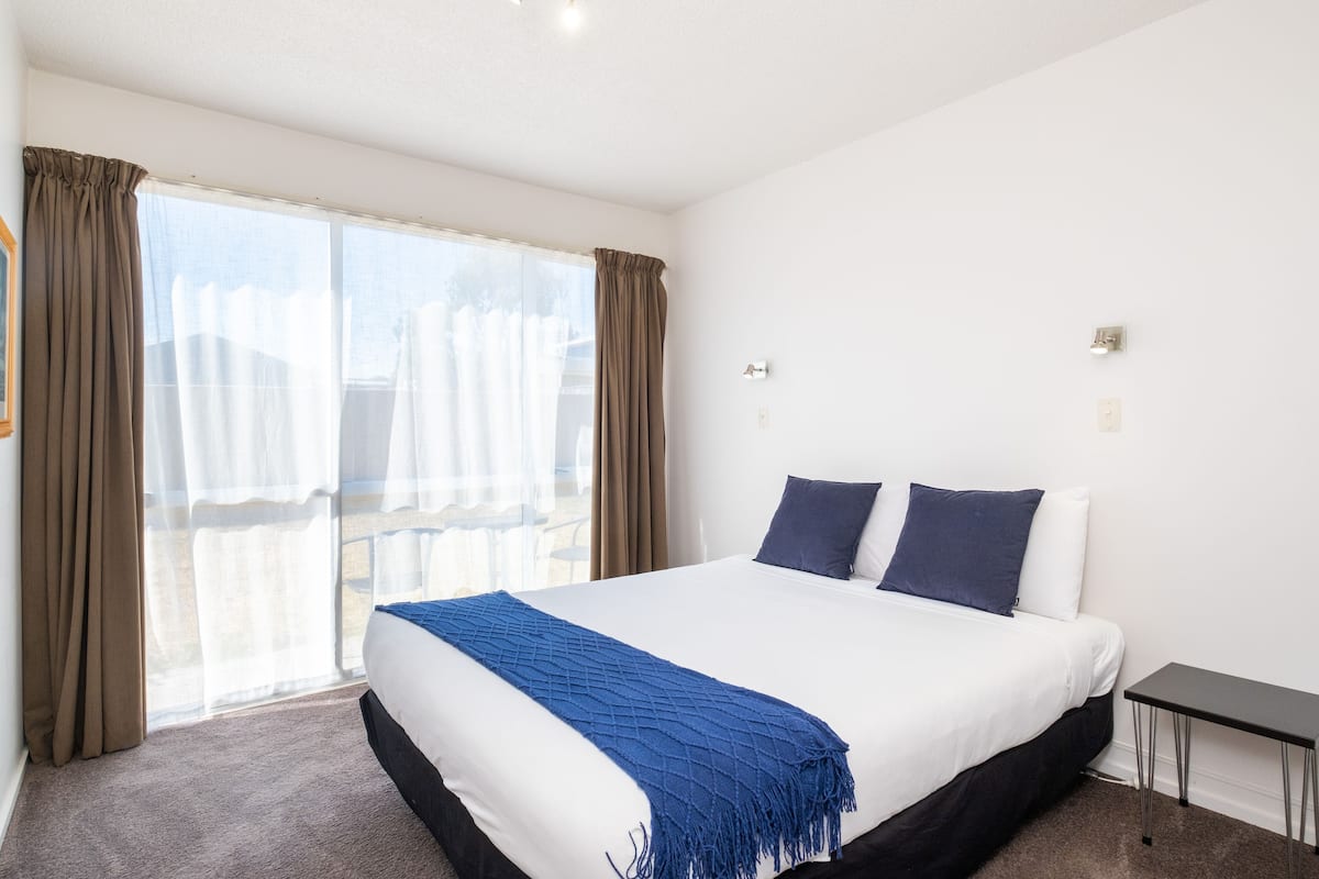 A hotel room with a large bed, a small table, and a view of a balcony.